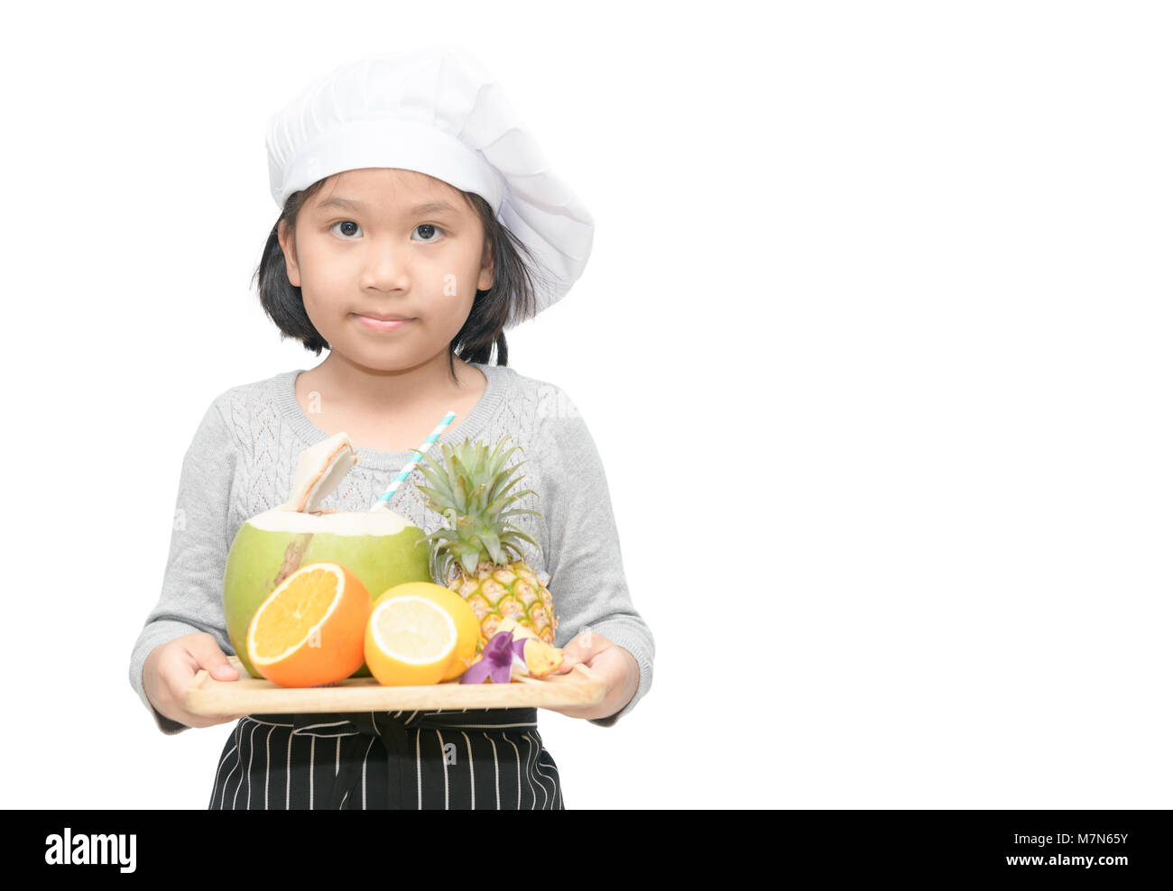 Ritratto di ragazza carina chef con un mix di frutta, arancio, noce di cocco e ananas e cuocere hat, grembiule stand e sorriso isolati su sfondo bianco Foto Stock