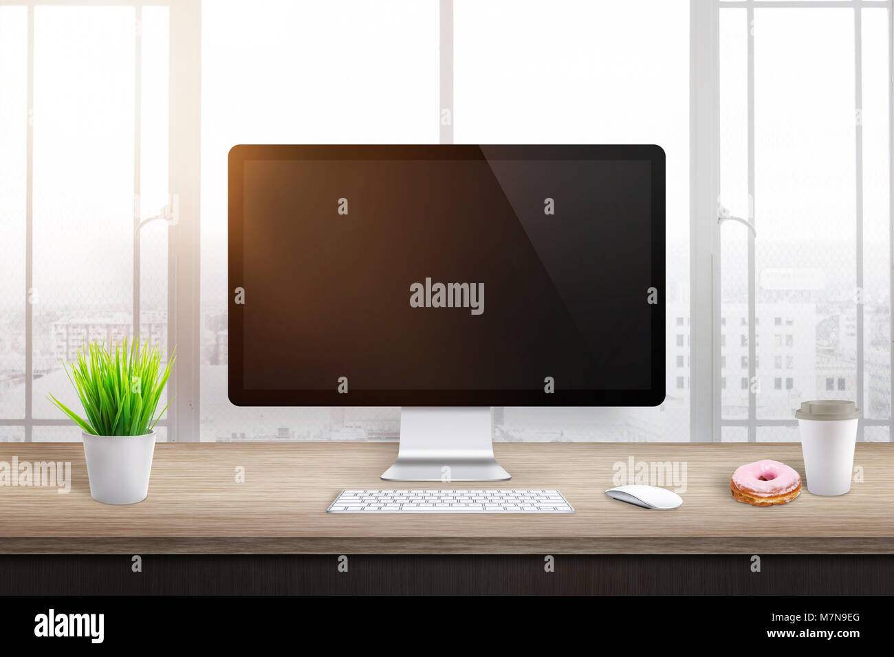 Vuoto il display del computer in ufficio o sul posto di lavoro. Impianto, caffè e ciambelle accanto a. Sole di mattina la luce in background. Foto Stock