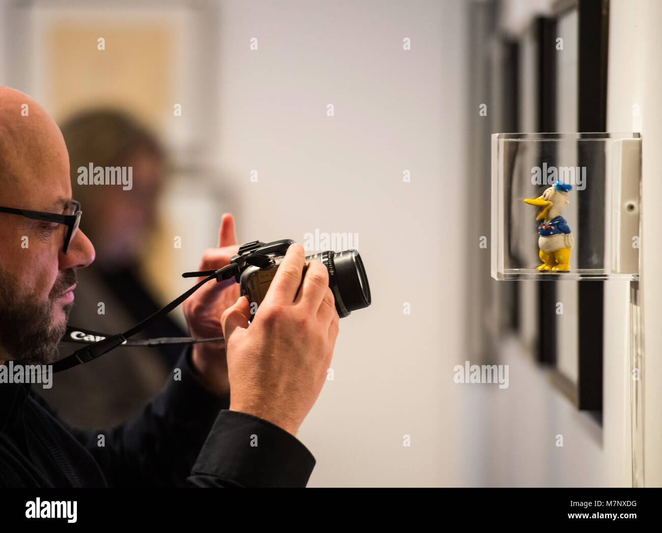 12 marzo 2018, Germania Mainz: Un fotografo scatta una foto di un Donald porcellana Durck figura dal 1930 alla mostra speciale 'Walt Disney - Mickey, Donald & Friends" presso il museo di stato. La mostra consente di visualizzare una panoramica dei caratteri' sviluppo dal progetto per il fumetto finito, come pure il metodo di lavoro degli illustratori. Foto: Andreas Arnold/dpa - ATTENZIONE: solo uso editoriale in connessione con la copertura più recenti su 'Walt Disney - Mickey, Donald & Friends" e solo se il credito sopra menzionato è a cui si fa riferimento nel pieno Foto Stock