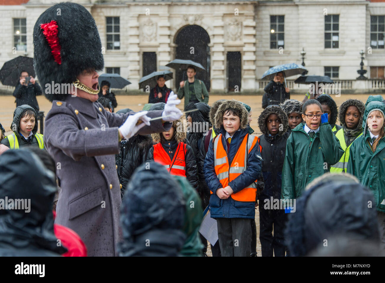Londra, Regno Unito. Xii marzo, 2018. Principali Simon Haw MBE, direttore di musica, conduce e incoraggia il canto - la banda delle guardie di Coldstream accompagna 400 membri del Commonwealth coro dei bambini in un musical celebrazione della Giornata del Commonwealth 2018. Le prestazioni, sulla sfilata delle Guardie a Cavallo, incluso un mondo prima di una nuova composizione, "per essere un amico", dedicata a Sua Maestà la Regina (e marcatura i capi di governo del Commonwealth riuniti (CHOGM) che si terrà a Londra nel mese di aprile 2018). Essa è stata composta da grandi Simon Haw MBE. Credito: Guy Bell/Alamy Live News Foto Stock