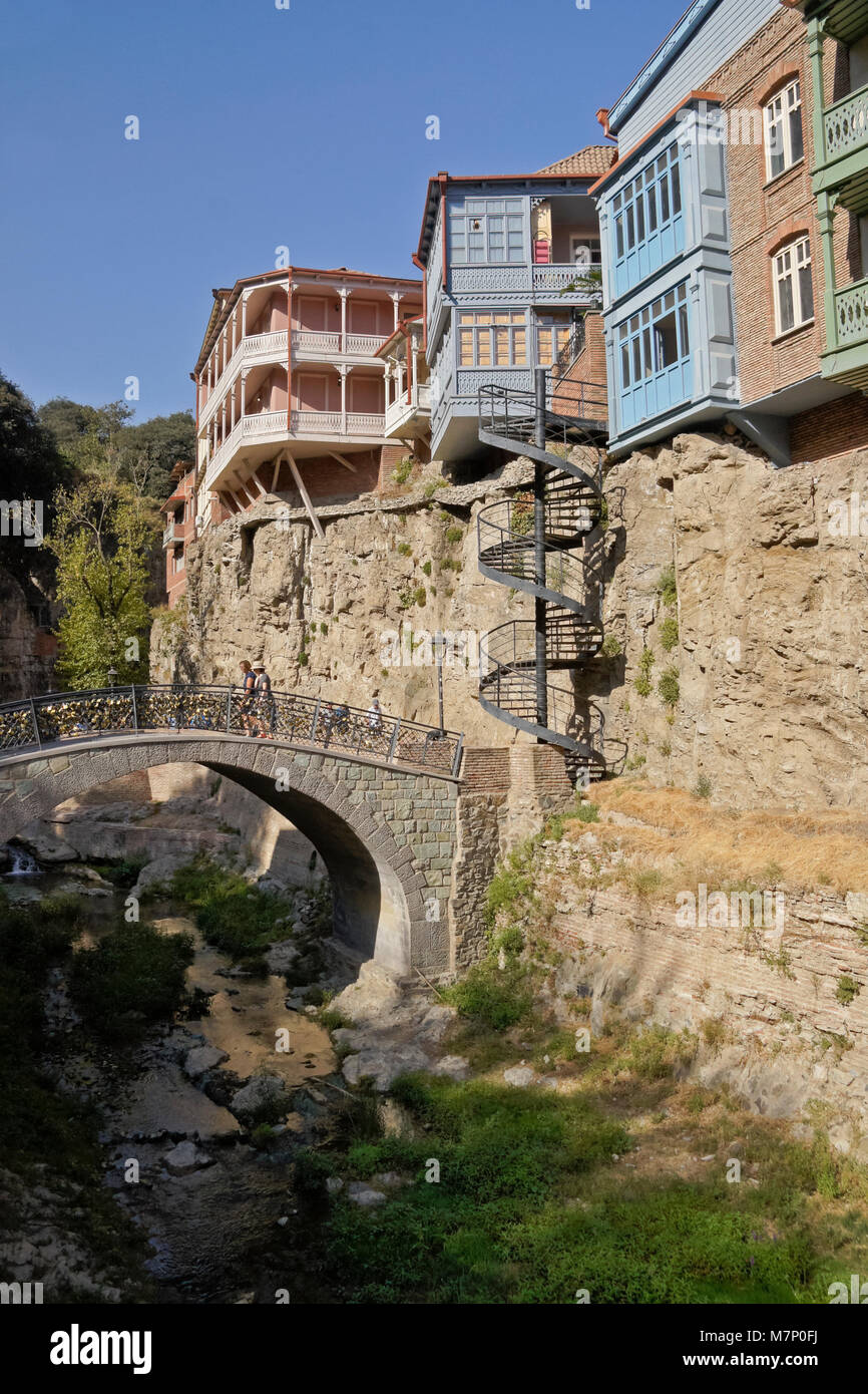 Vecchie case su una scogliera e un andamento arcuato ponte in pietra attraverso un ruscello, Tbilisi, Georgia Foto Stock