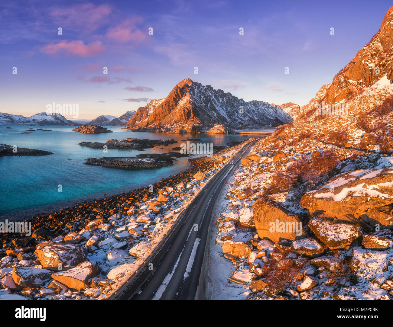Vista aerea della bella strada di montagna vicino al mare, montagne, viola il cielo al tramonto in isole Lofoten in Norvegia in inverno. Vista superiore della strada, auto, alta Foto Stock