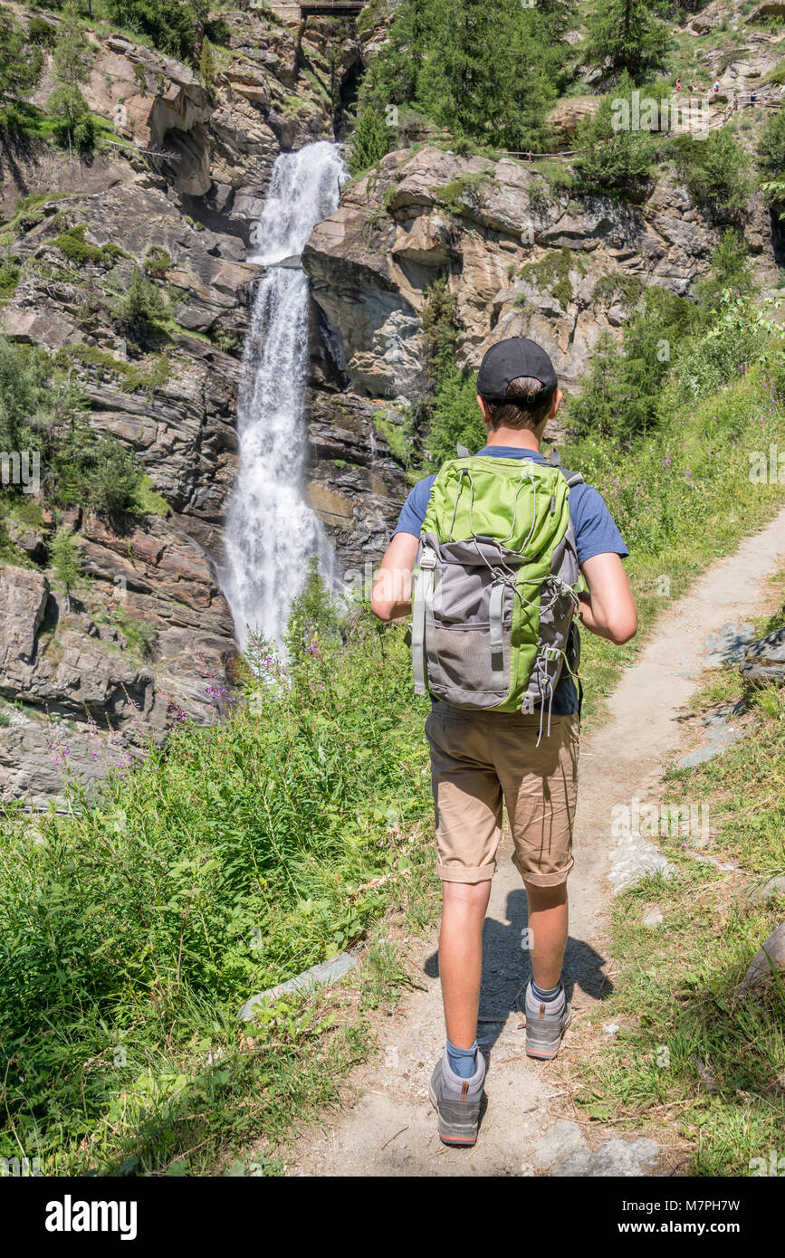 Giovane escursionista con zaino su un sentiero di montagna, cascate di Lillaz vicino a Cogne, il parco nazionale del Gran Paradiso, Valle d'Aosta nelle Alpi, Italia Foto Stock