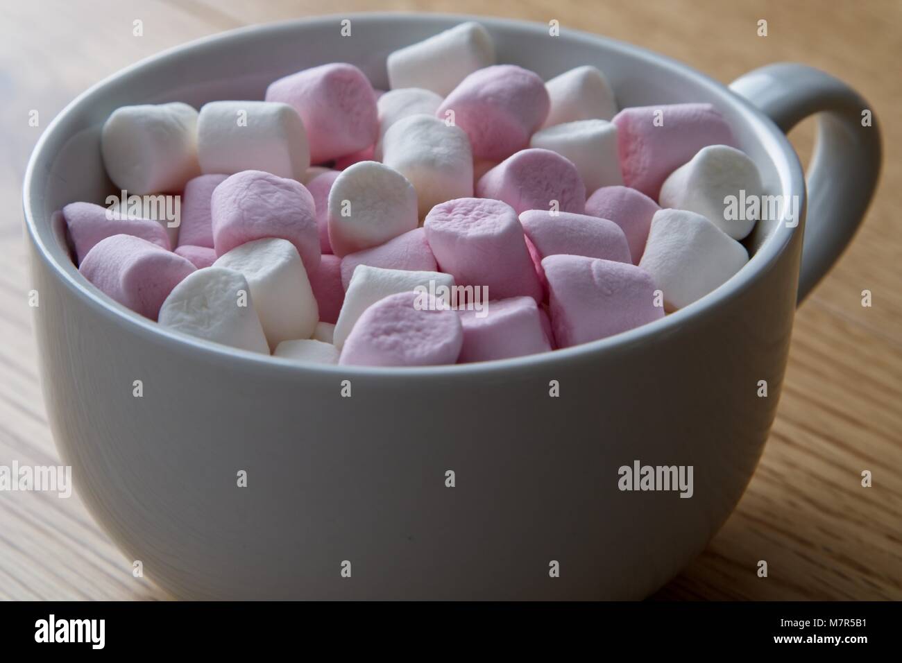 Tazza bianca contenente rosa e bianco miniatura marshmallows sulla superficie di quercia Foto Stock