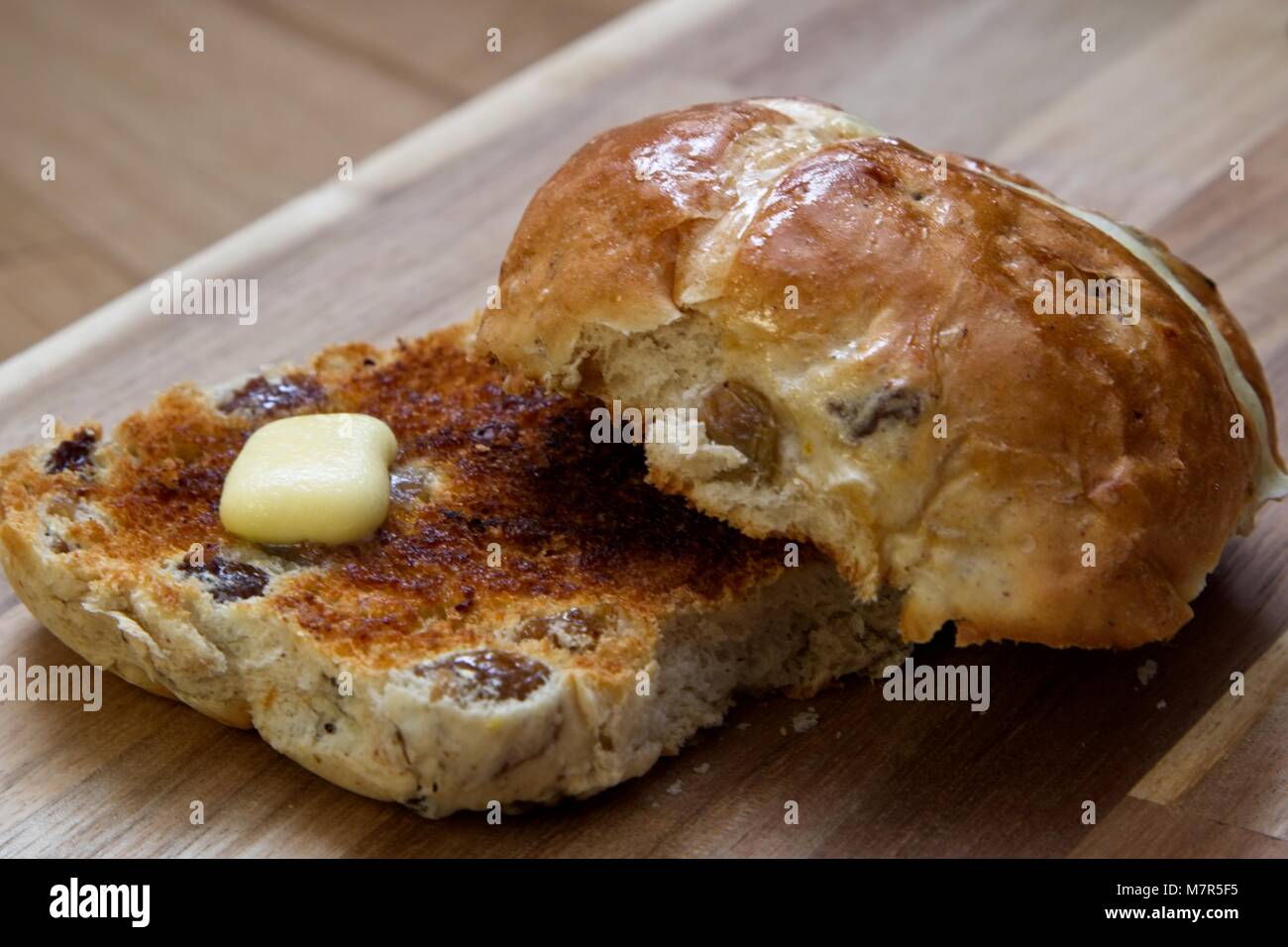 Vista laterale di pane abbrustolito hot cross bun con burro di fusione su legno scheda servente Foto Stock