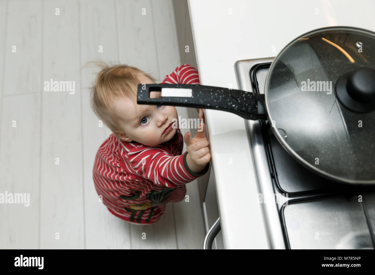 Sicurezza dei bambini a casa concetto - toddler raggiungendo per la coppa sui fornelli in cucina Foto Stock