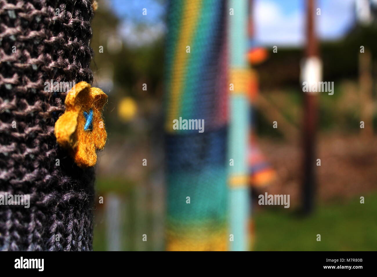 Maglieria colorata con un fiore giallo attorno al vecchio poli elettrici a Oban, Scozia. Foto Stock