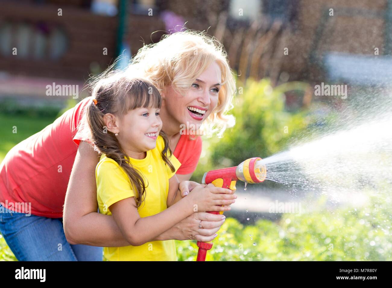 Pretty Woman e sua figlia di innaffiamento con tubo flessibile in giardino Foto Stock