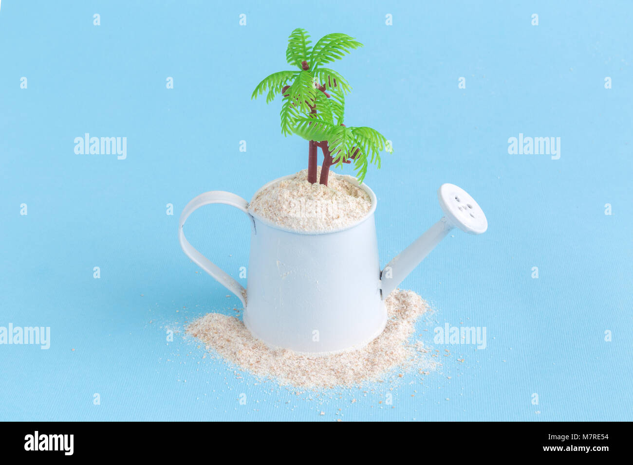 Piccolo annaffiatoio pieno di sabbia con Palm tree contro pastello blu sullo sfondo. Estate vacanze viaggi la minima nozione. Foto Stock