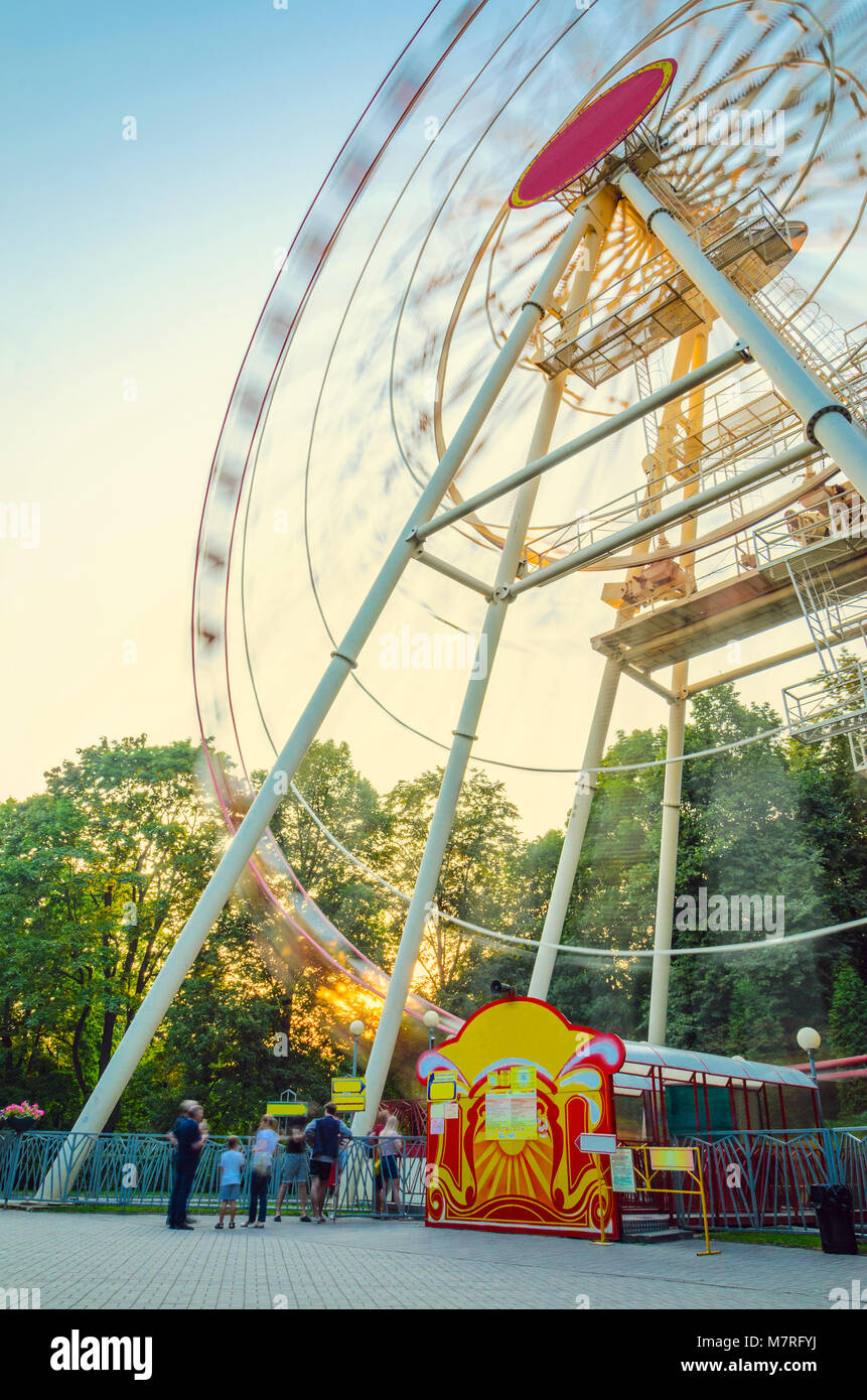 Sfumata in Motion sagome di persone in piedi in linea per la ruota panoramica nel parco dei divertimenti al tramonto. Una lunga esposizione paesaggio nel Amusemen Foto Stock