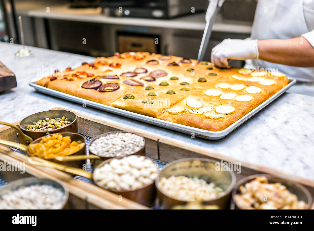 Ristorante Cucina foccacia di taglio il pane con il coltello, noci, spezie in contenitori e condimenti uomo chef dopo la cottura in forno Foto Stock