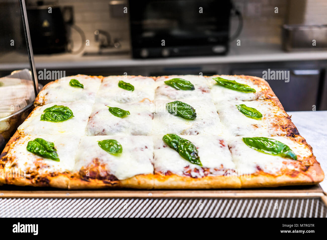 Primo piano della mozzarella foccacia pane con il verde del basilico in foglie, formaggio fuso pizza dopo la cottura, golden crosta marrone sul tavolo da cucina Foto Stock
