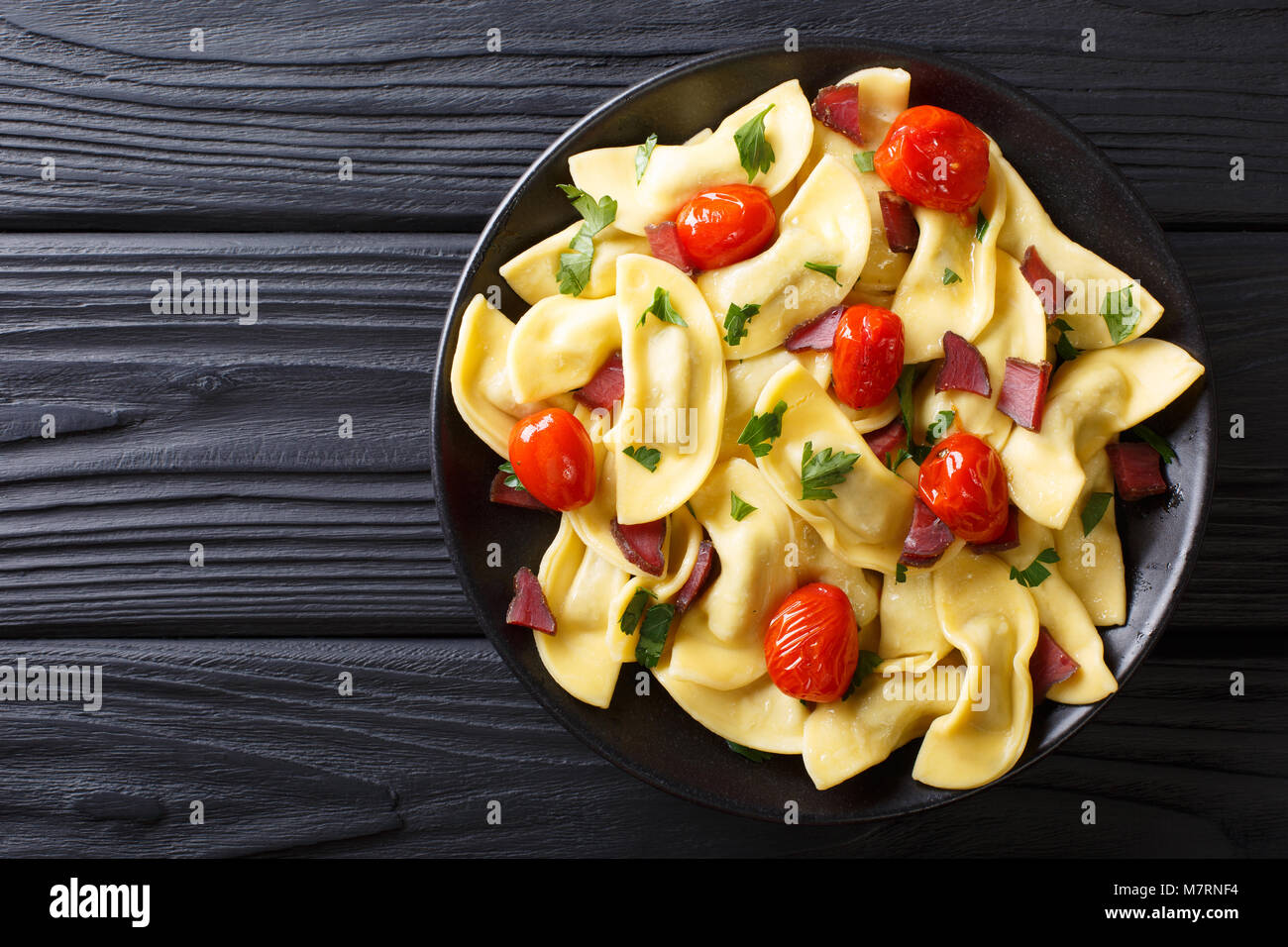 Gnocchi italiano casoncelli ripieni di prosciutto crudo con pomodorini close-up su una piastra sul tavolo. parte superiore orizzontale vista da sopra Foto Stock