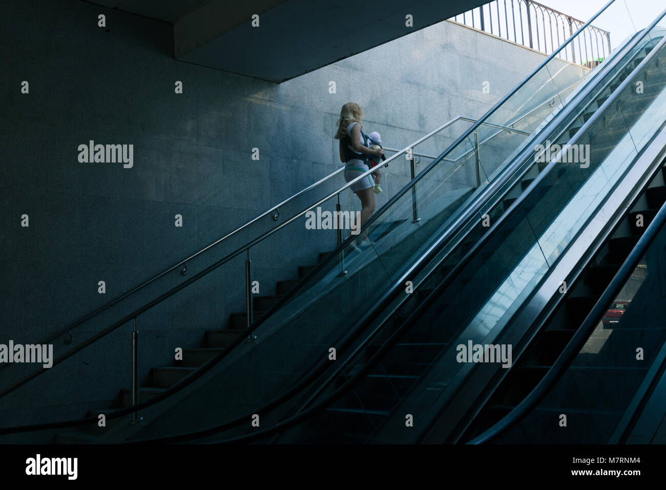 Moderna madre con bambino toddler nel passaggio urbano con luce drammatica Foto Stock