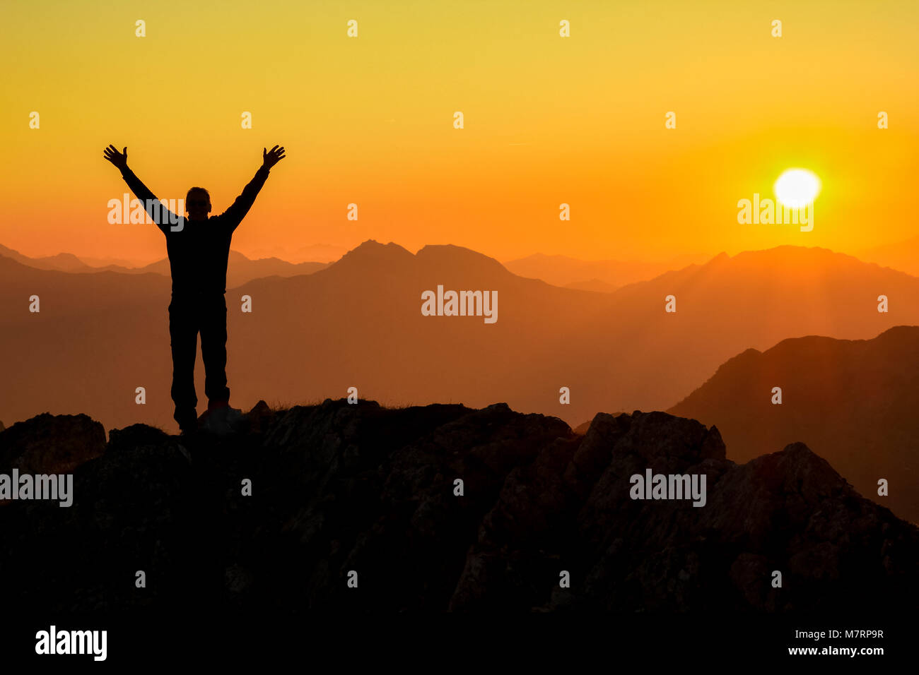 Felice celebra il successo vincendo l uomo al tramonto o l'alba euforico in piedi con le braccia sollevate fino sopra la sua testa nella celebrazione di aver raggiunto mountai Foto Stock