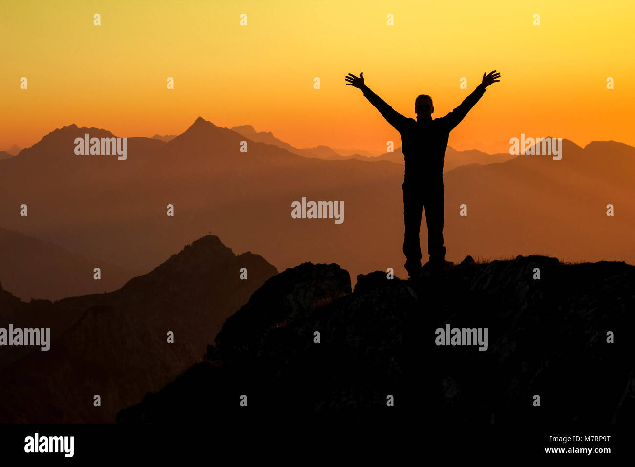 Felice celebra il successo vincendo l uomo al tramonto o l'alba euforico in piedi con le braccia sollevate fino sopra la sua testa nella celebrazione di aver raggiunto mountai Foto Stock