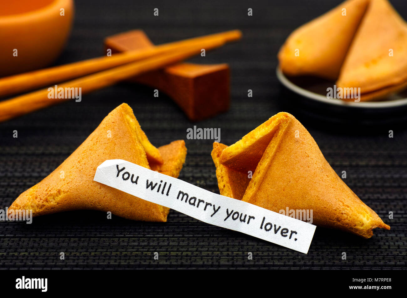 La striscia di carta con la frase che si sposerà il tuo amante da Fortune cookie, un altro biscotto e bacchette sul tovagliolo nero lo sfondo. Foto Stock