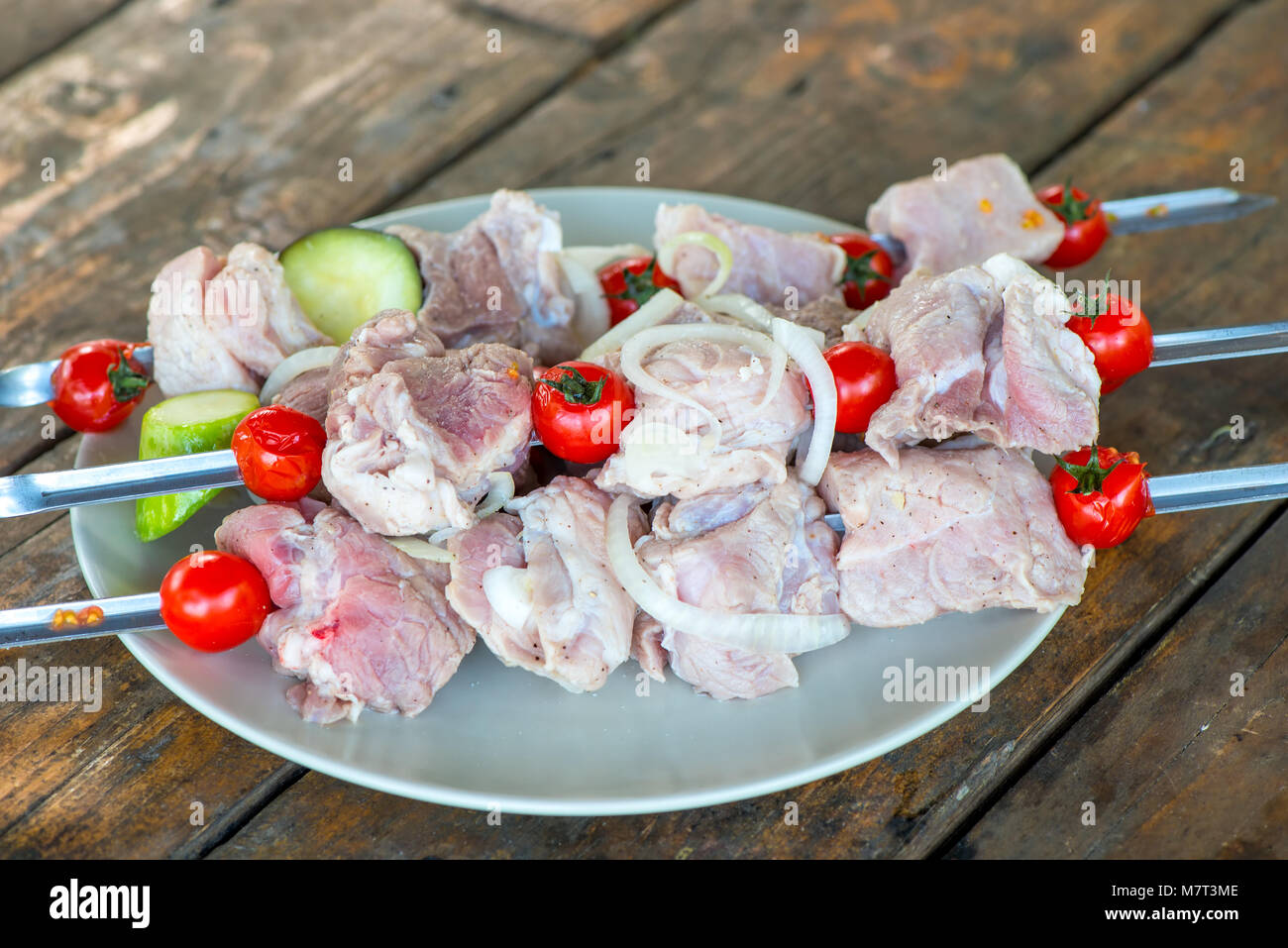 Marinata di shish kebab spiedini su giace su una piastra su un tavolo di legno prima della frittura Foto Stock