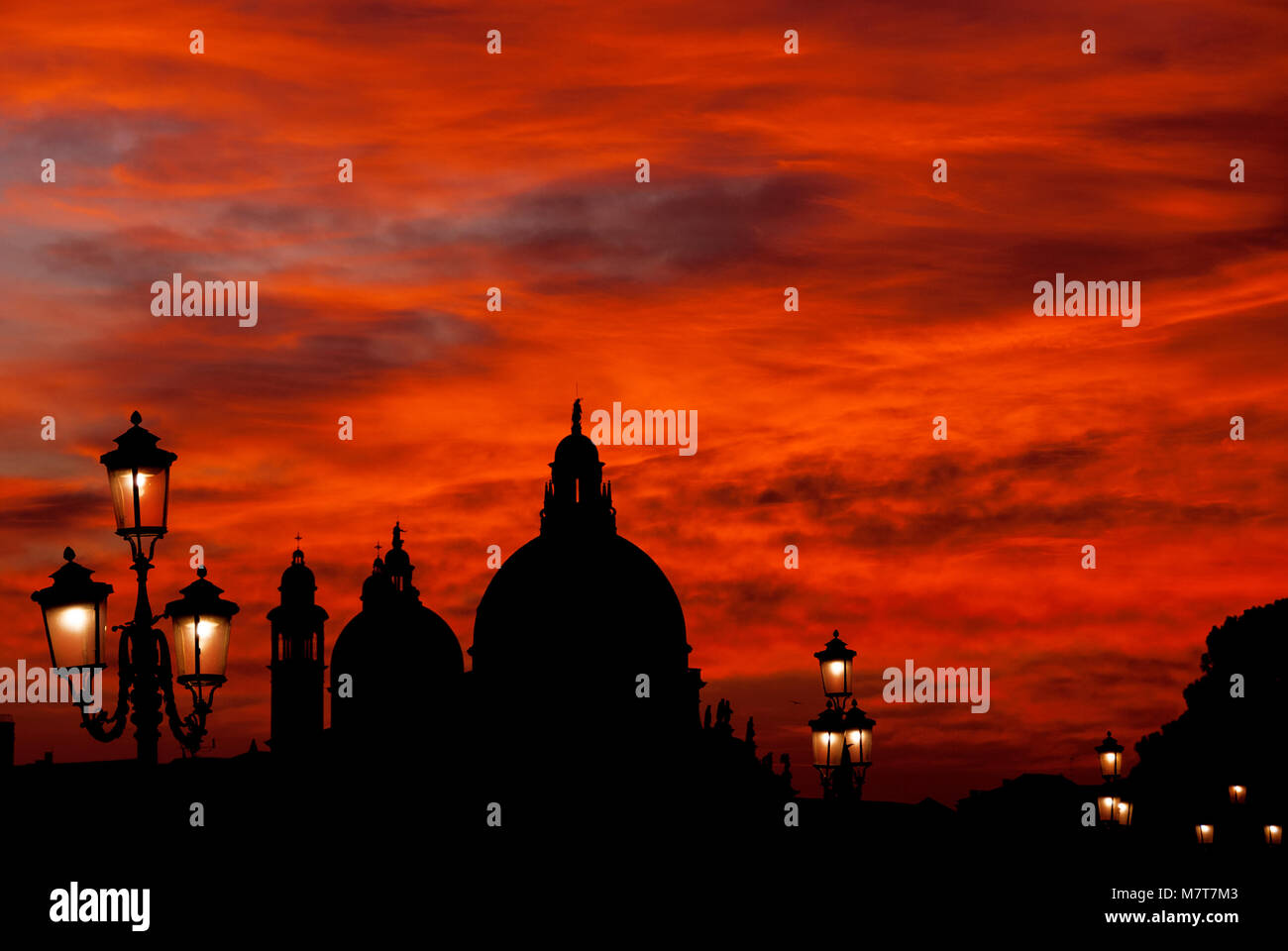 Rosso Sangue sky tramonto sulla laguna di Venezia con la Basilica salutano le cupole e vecchie lampade Foto Stock