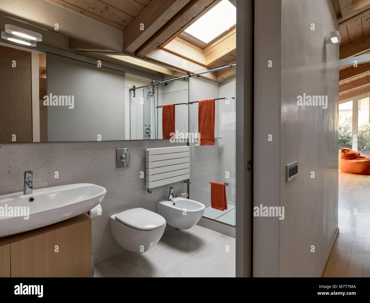 In primo piano il contatore top lavabo, wc e bidet in background sotto il lucernario il box doccia in vetro Foto Stock