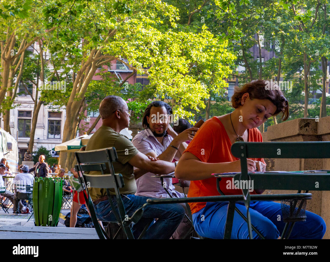Una donna che scrive ad un tavolo in Bryant Park New York mentre due uomini dietro di lei su un altro tavolo stanno avendo una conversazione, Bryant Park, New York Foto Stock