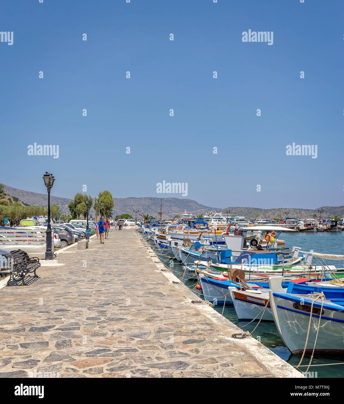 Una passeggiata in Elounda, Creta, si estende nella distanza. Una miriade di piccole barche da pesca sono ormeggiate su un lato. Foto Stock