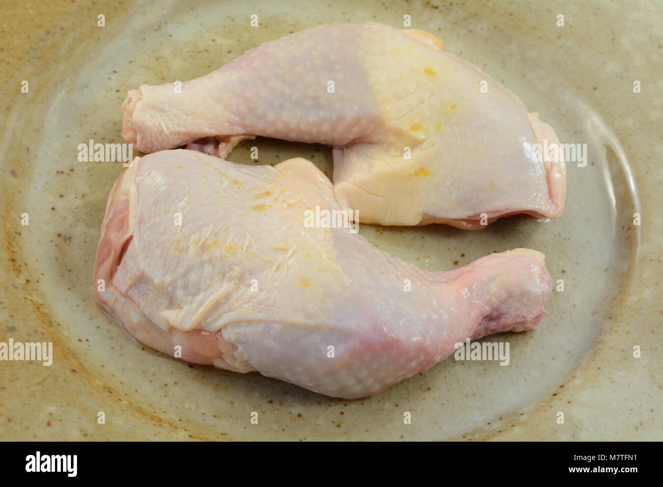 Due nuove materie le cosce di pollo con la pelle su rustiche piastra ceramica in preparazione o cena di cucina Foto Stock