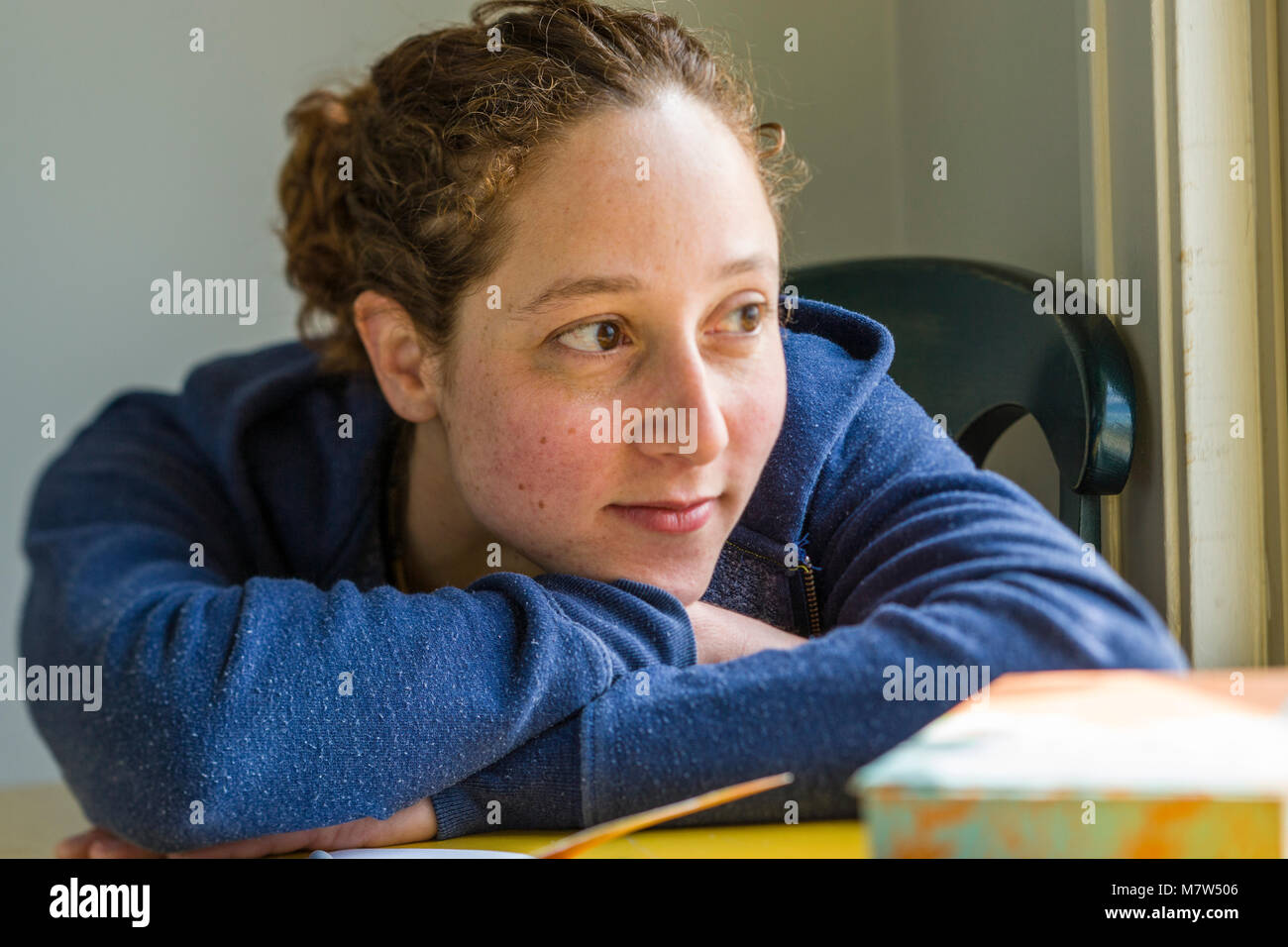 Ritratto di una giovane donna con il suo capo sulle sue braccia mentre si è seduti ad un tavolo. Foto Stock