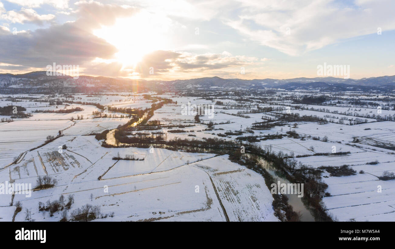 Vista aerea del fiume che scorre attraverso la coperta di neve la campagna al tramonto. Foto Stock