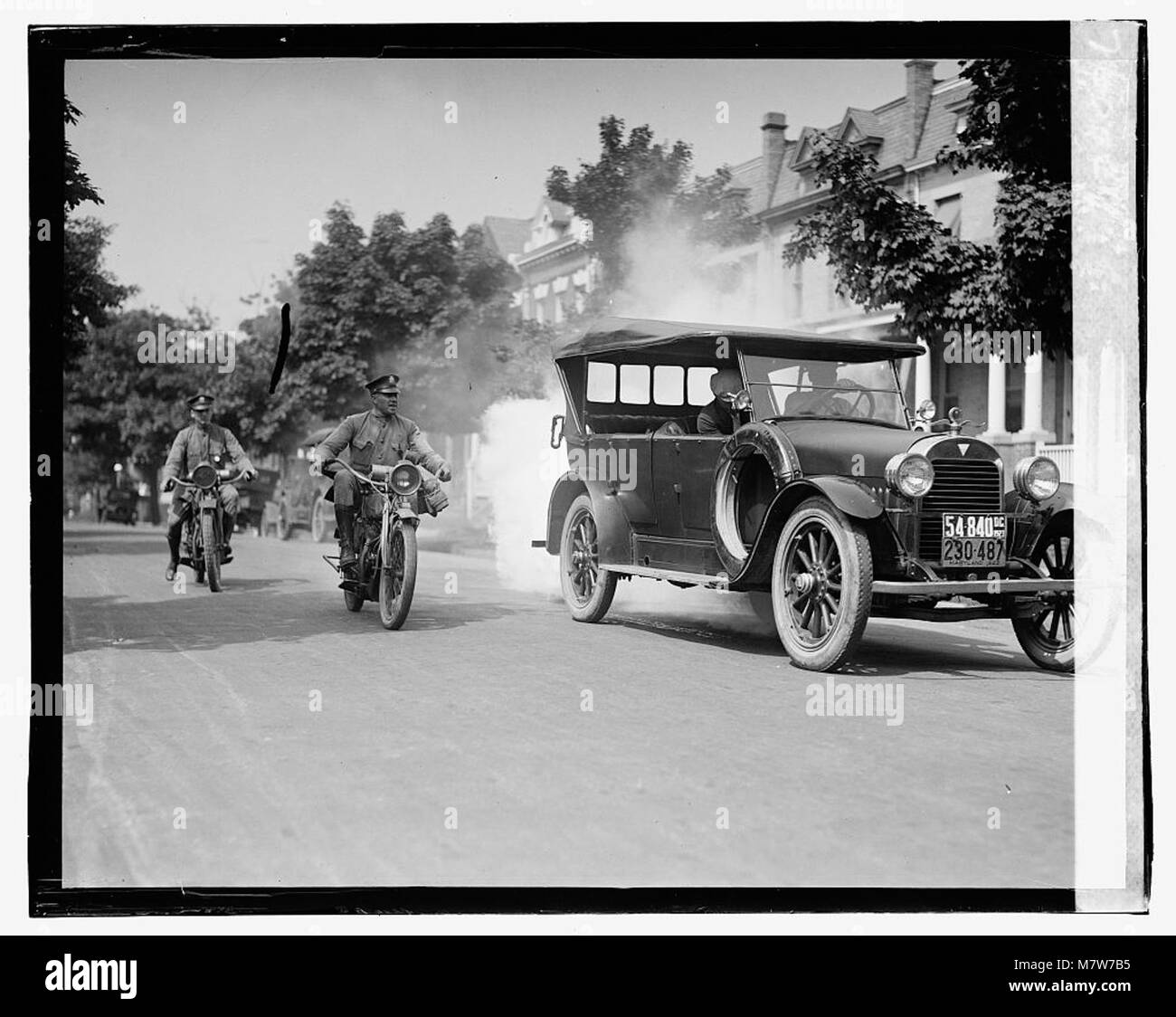 Questa fotografia cattura una scena con la polizia in moto che segue un'auto che emette fumo, documentando un momento storico nelle attività delle forze dell'ordine il 1° settembre 1923. Foto Stock