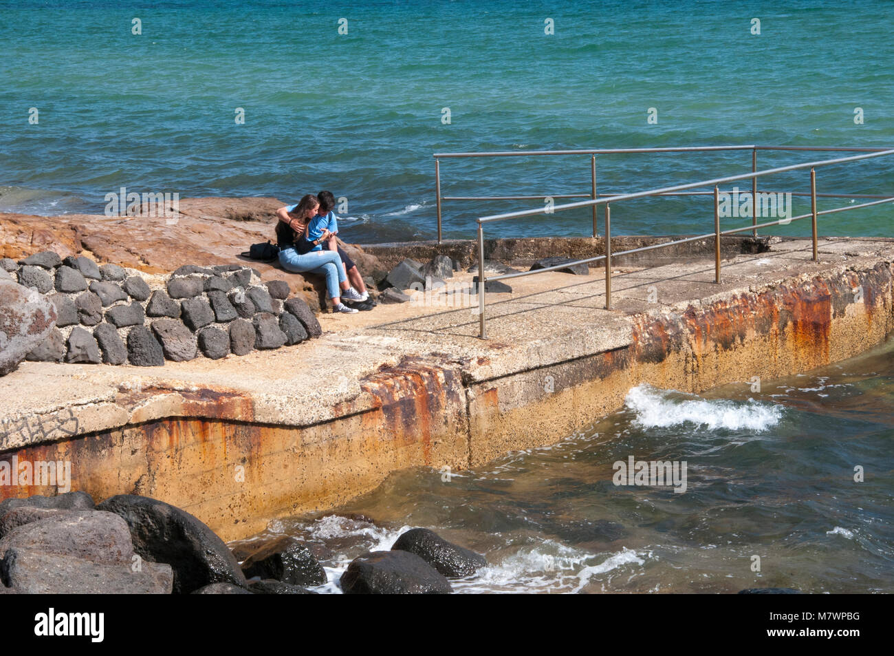 Adolescente matura la condivisione di un intimo momento su un frangiflutti a Long Beach a Parkdale, Melbourne, Australia Foto Stock