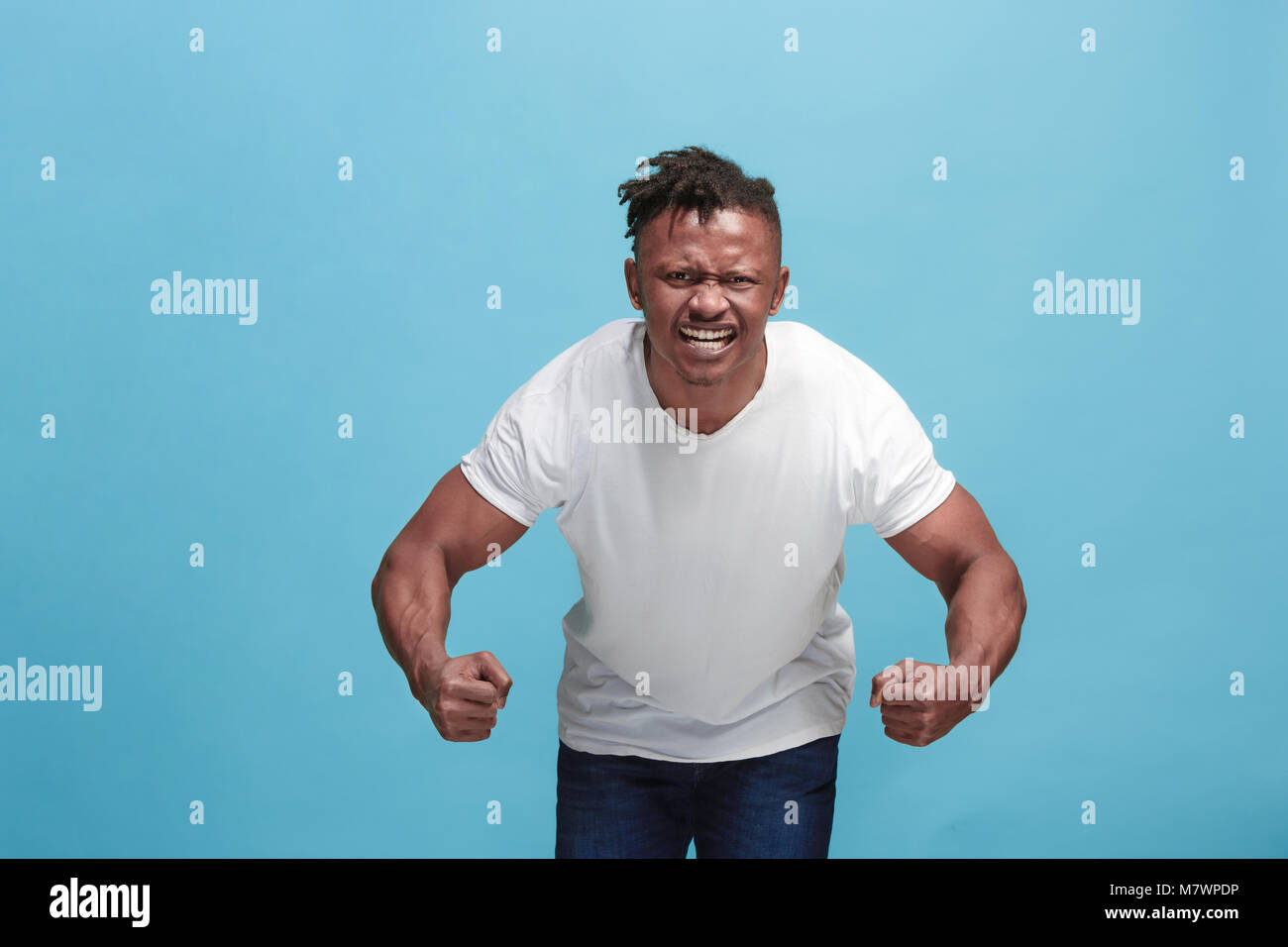 Il giovane arrabbiato emotivo afro uomo urlando su blu di sfondo per studio Foto Stock