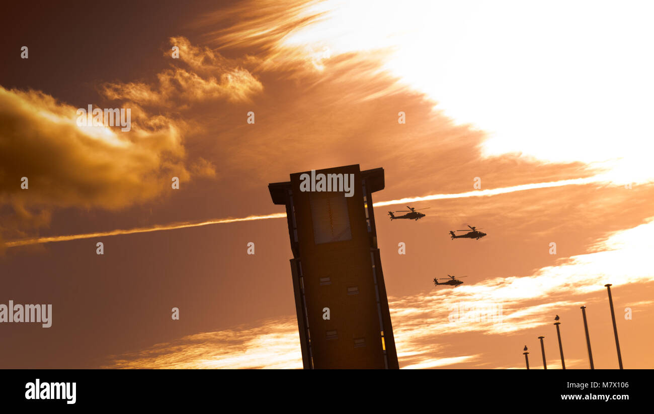 Tre elicotteri Apache volare oltre la torre con la masterizzazione di cielo arancione Foto Stock