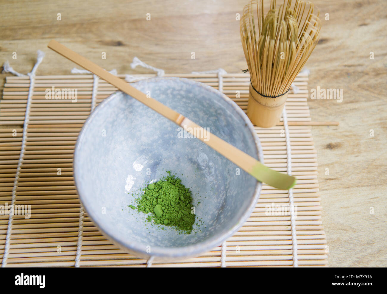 Al di sopra di vista della cerimonia del tè giapponese elementi comprendenti un recipiente in pietra di tè verde Matcha in polvere, una frusta di bambù e bambù scoop su una stuoia di bambù. Foto Stock