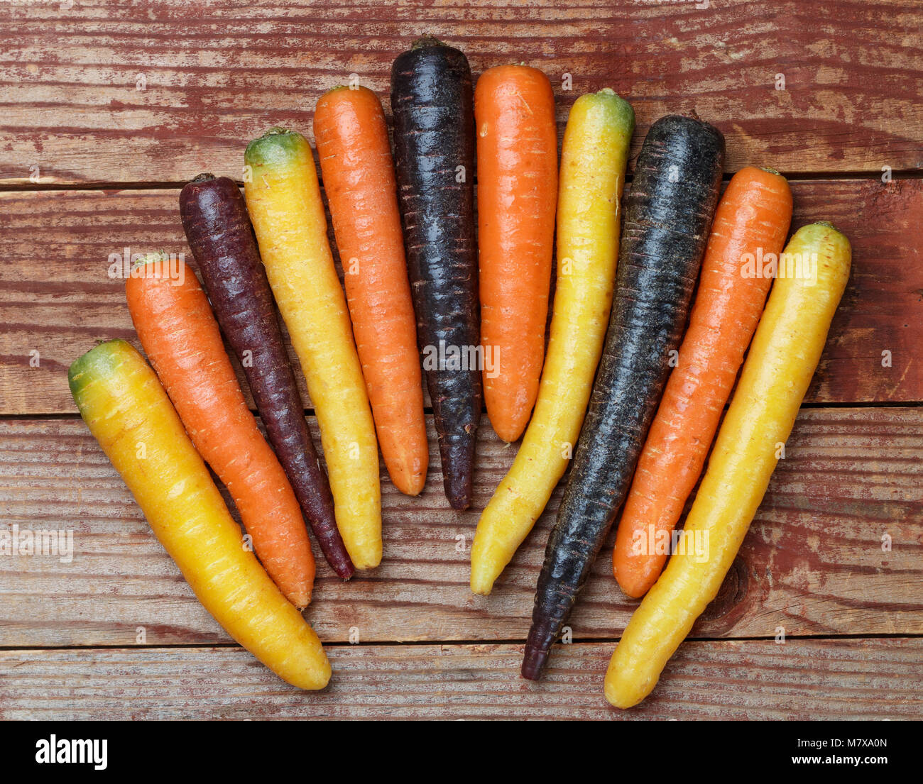 Verdure colorate. Organici di colore giallo, rosso, arancione e viola le carote su una tavola di legno. Stile rustico Foto Stock