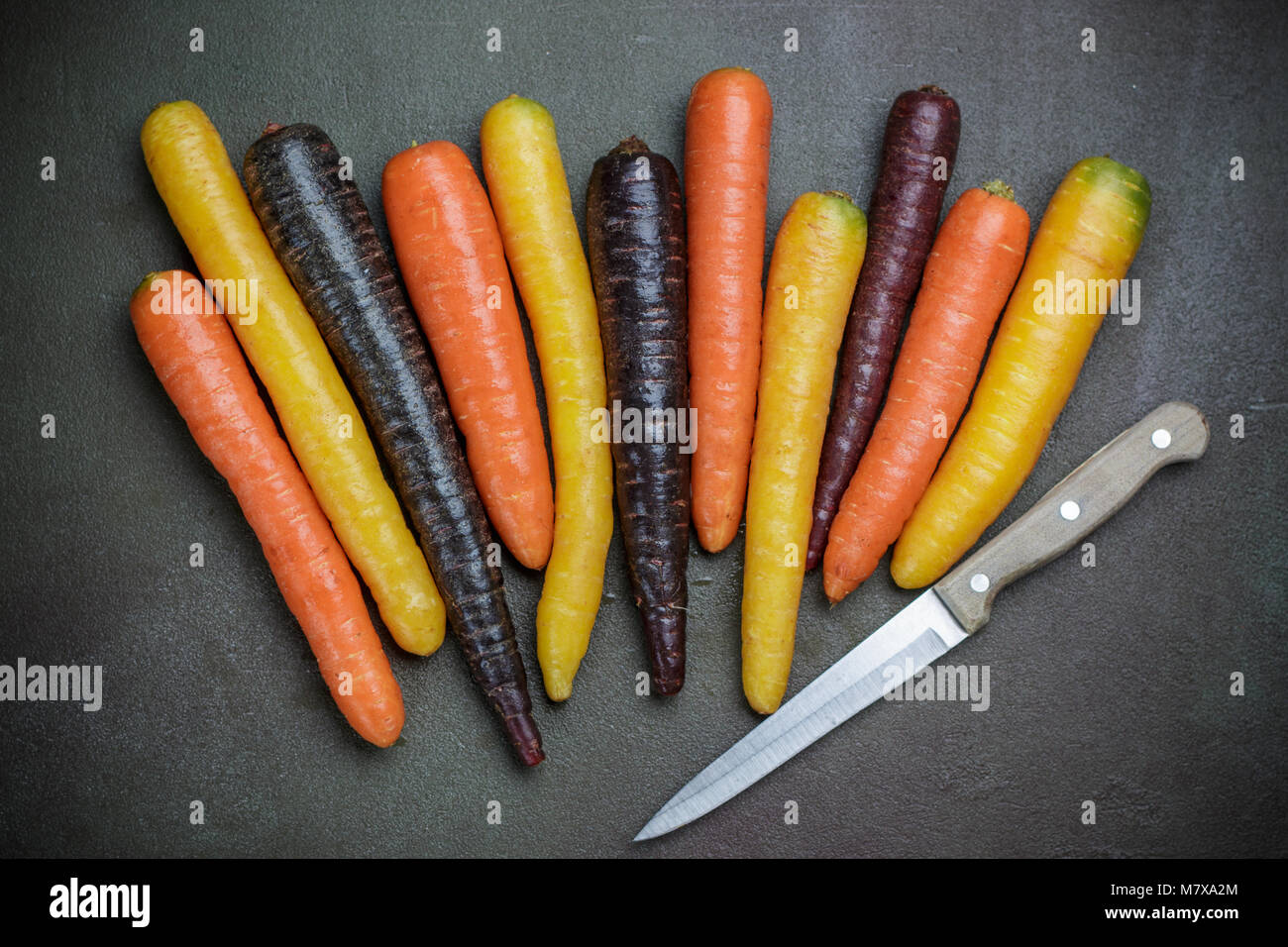 Verdure colorate. Organici di colore giallo, rosso, arancione e viola le carote in pietra scura superficie. Stile rustico Foto Stock