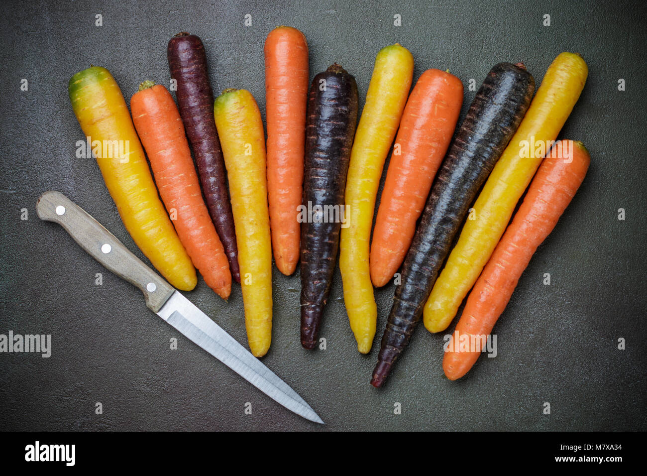 Verdure colorate. Organici di colore giallo, rosso, arancione e viola le carote in pietra scura superficie. Stile rustico Foto Stock