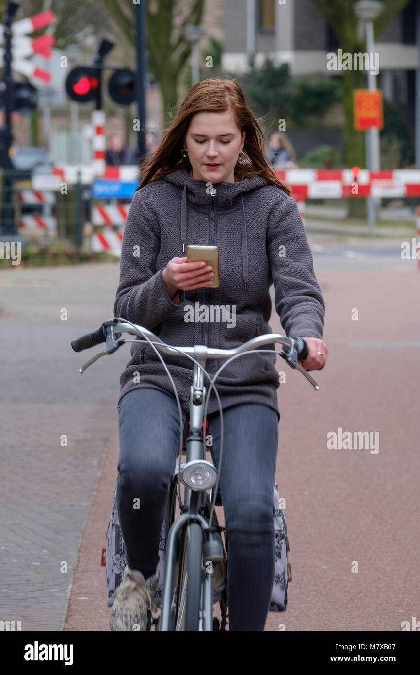 Giovane donna getting distratto dal suo smartphone mentre in sella alla sua bicicletta in giro per la città Foto Stock