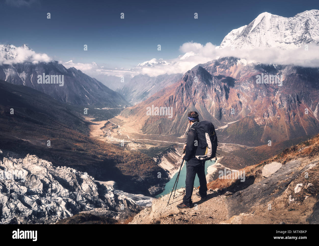 In piedi sportivo da uomo con zaino sul picco di montagna e bellissime montagne atbright giornata di sole. Paesaggio con uomo, rocce con vette innevate, ghiacciaio Foto Stock