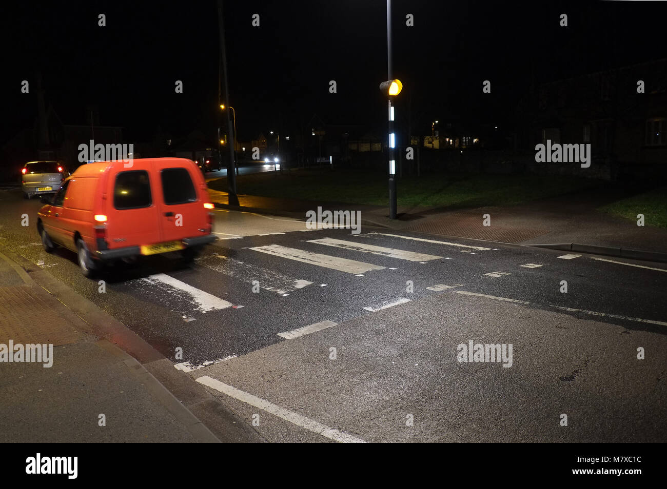 Gennaio 2018 - Villaggio zebra attraversamento su strada di notte con un vecchio rosso van passante Foto Stock