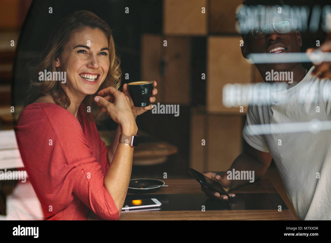 Donna sorridente seduti ad un tavolo da caffè tenendo una tazza di caffè. Donna sorridente seduto con il suo amico in una caffetteria. Foto Stock
