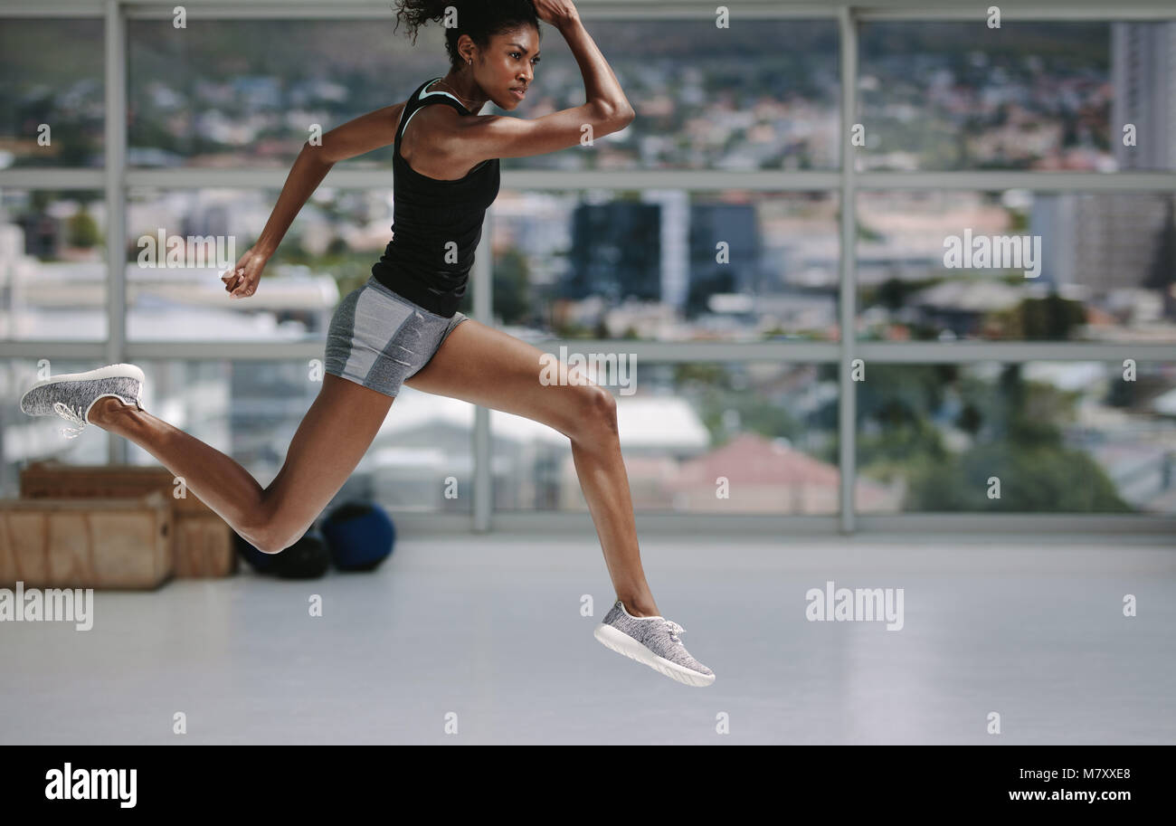 Femmina con slim figura correre e saltare nel fitness studio. Un sano donna africana che lavora fuori all'interno. Foto Stock