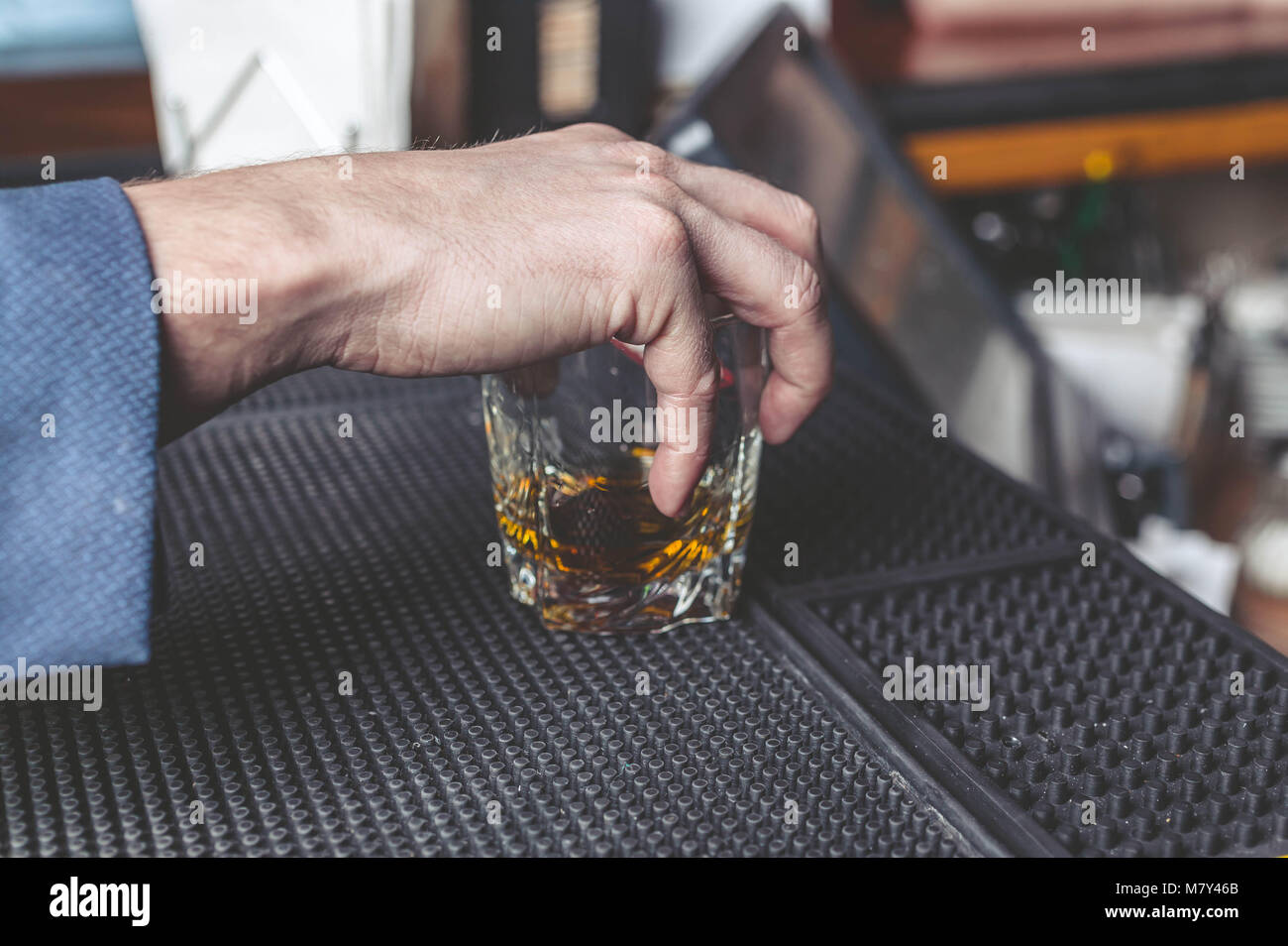 Il maschio di mano trattiene un bicchiere da whisky su un banco di bar Foto Stock