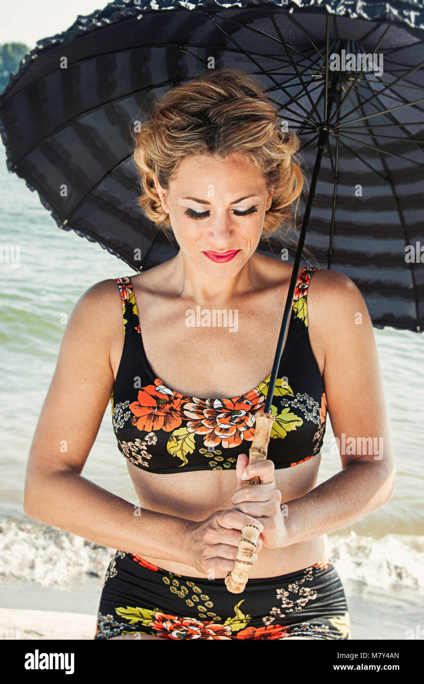 Una donna in costume da bagno, in piedi sulla spiaggia con un ombrello vintage. Foto Stock