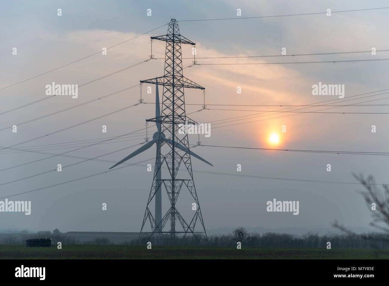 Turbina eolica e traliccio di elettricità al tramonto Foto Stock