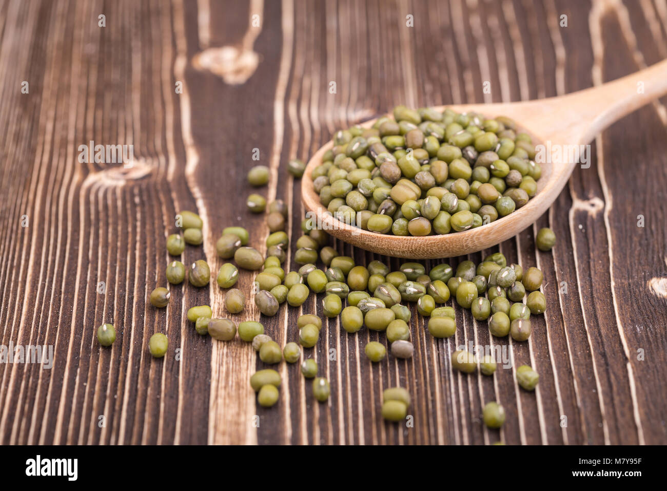 Close up Mung bean in cucchiaio di legno messo sul tavolato in legno sfondo Foto Stock