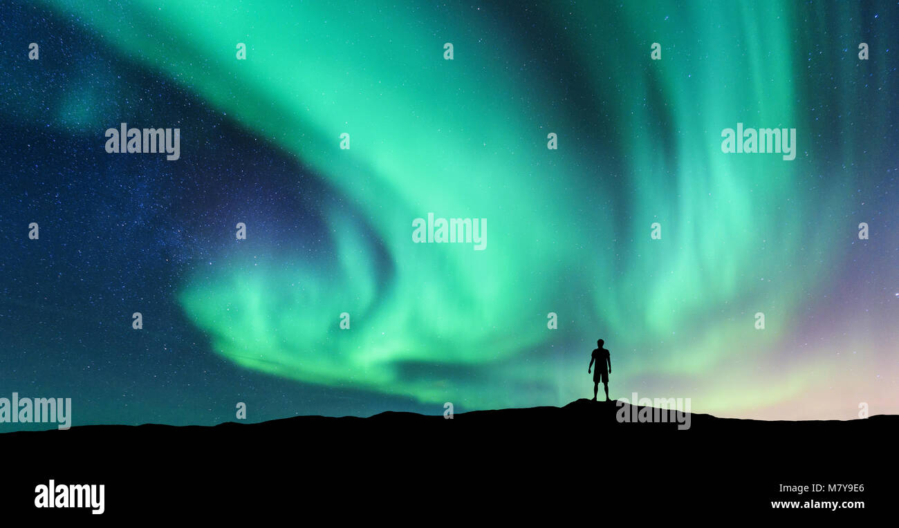 Aurora boreale e silhouette di un uomo in piedi. Isole Lofoten in Norvegia. Aurora e uomo felice. Cielo con le stelle e verde luci polari. Paesaggio notturno Foto Stock