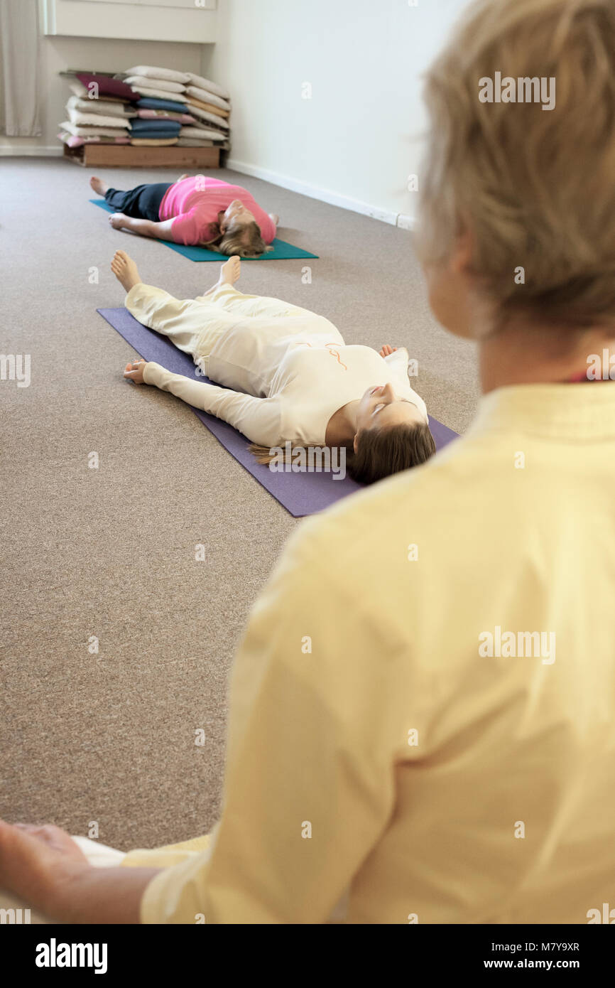 I giovani praticanti il relax anche chiamato yoga nidra. Guidati da una femmina certificate istruttore yoga posa in shavasana su theri appoggia sul materassino yoga Foto Stock