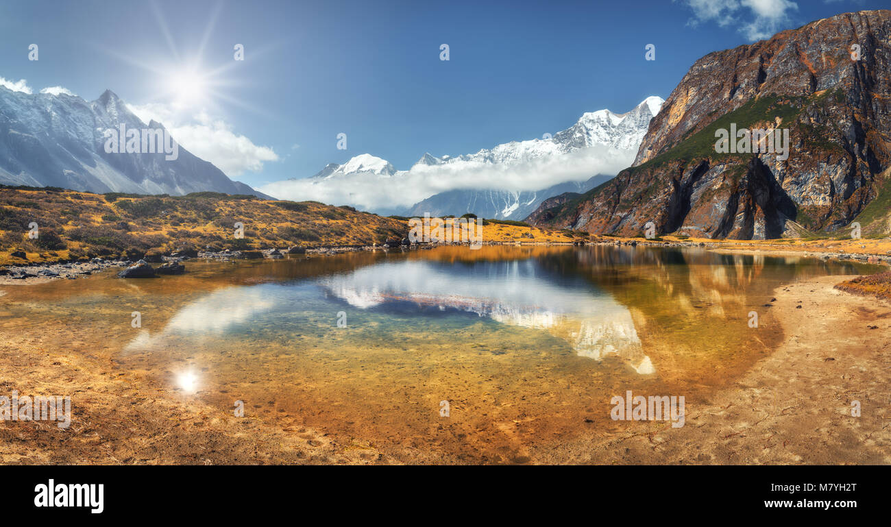 Bella scena con alte rocce con cime coperte di neve, lago di montagna e la riflessione in acqua, cielo blu con nuvole nel tramonto. Il Nepal. Landscap panoramica Foto Stock