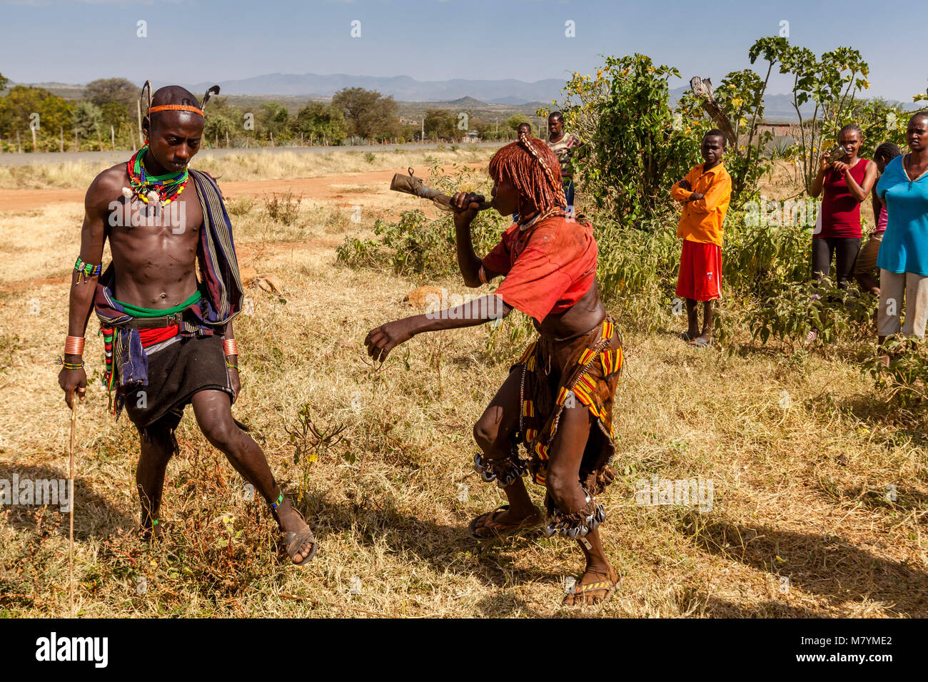 Giovani donne Hamar Taunt A Hamar Tribesman alla fustigazione essi durante un 'proveniente dall'età' Bull Jumping cerimonia, Dimeka, Valle dell'Omo, Etiopia Foto Stock